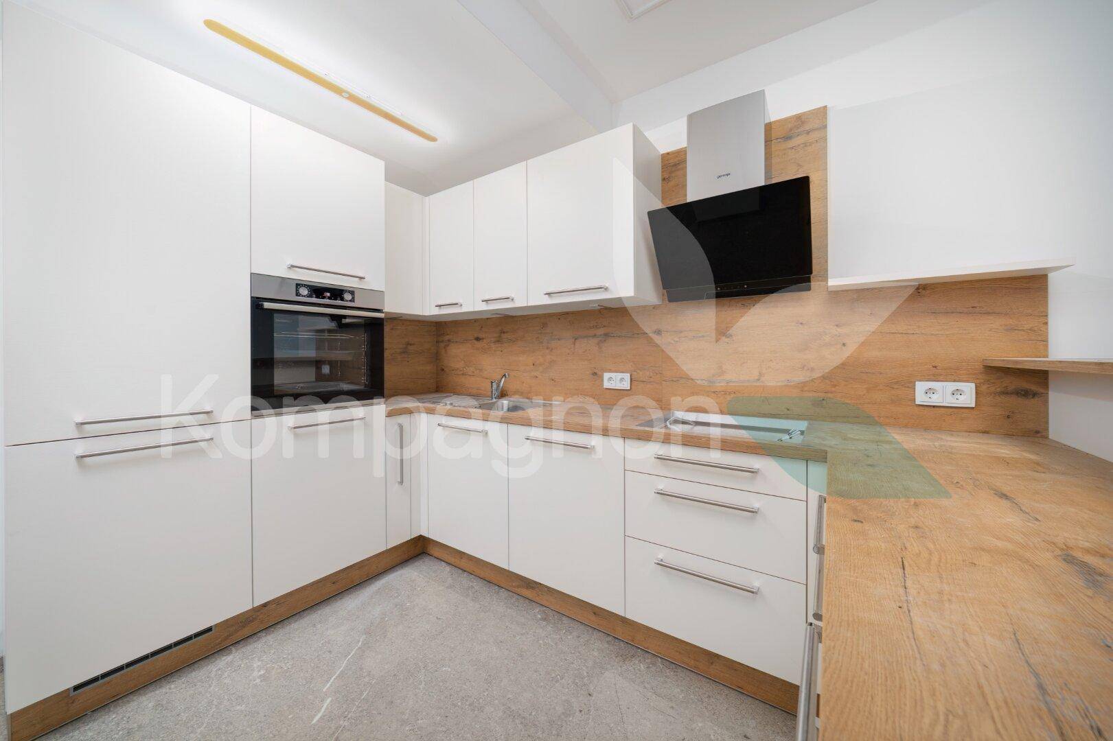 Moderne Einbauküche mit weißen Fronten, Holzakzenten und integriertem Backofen.