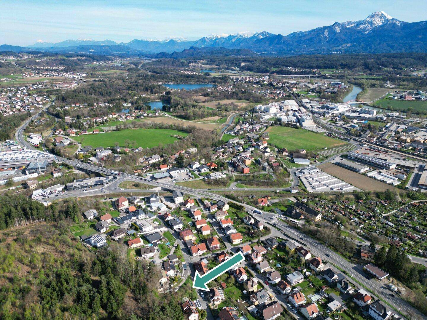 Weitläufige Luftaufnahme einer Wohngegend mit Wald, Seen und Bergen im Hintergrund.