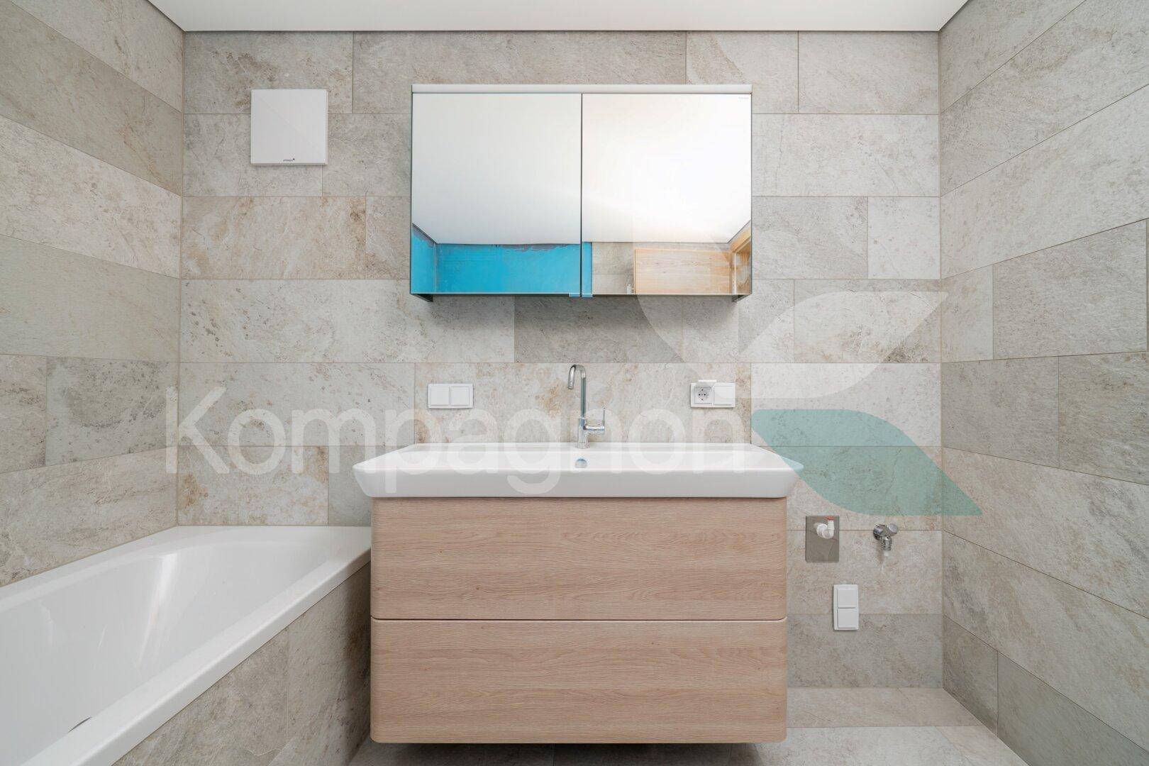 Modernes Badezimmer mit Badewanne, Holzwaschtisch und Spiegelschrank in hellen Grautönen.