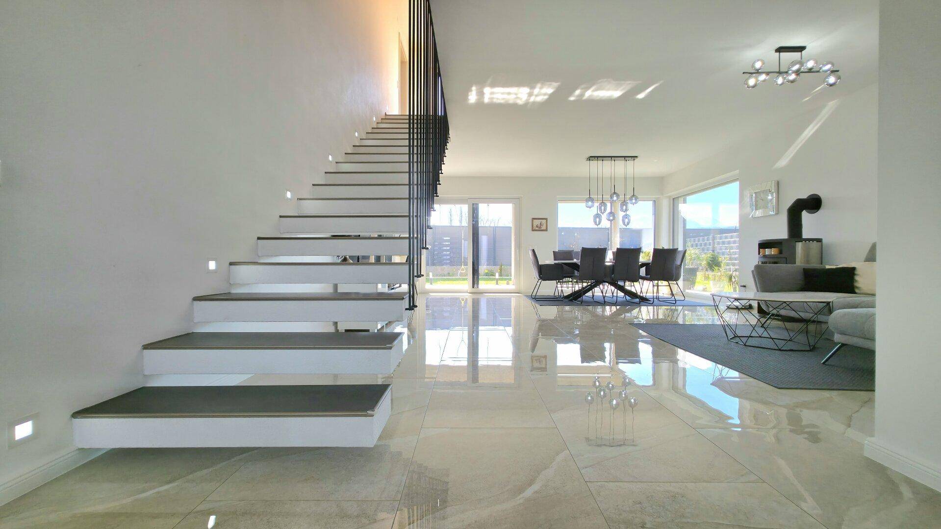 Heller Wohn- und Essbereich mit moderner Treppe, Kaminofen und Zugang zum Garten durch große Schiebetüren.