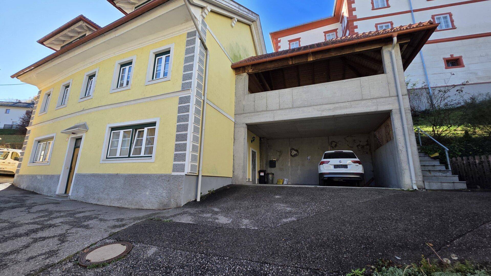 Traditionelles gelbes Haus mit überdachtem Parkplatz und Zugang zum Gebäude.