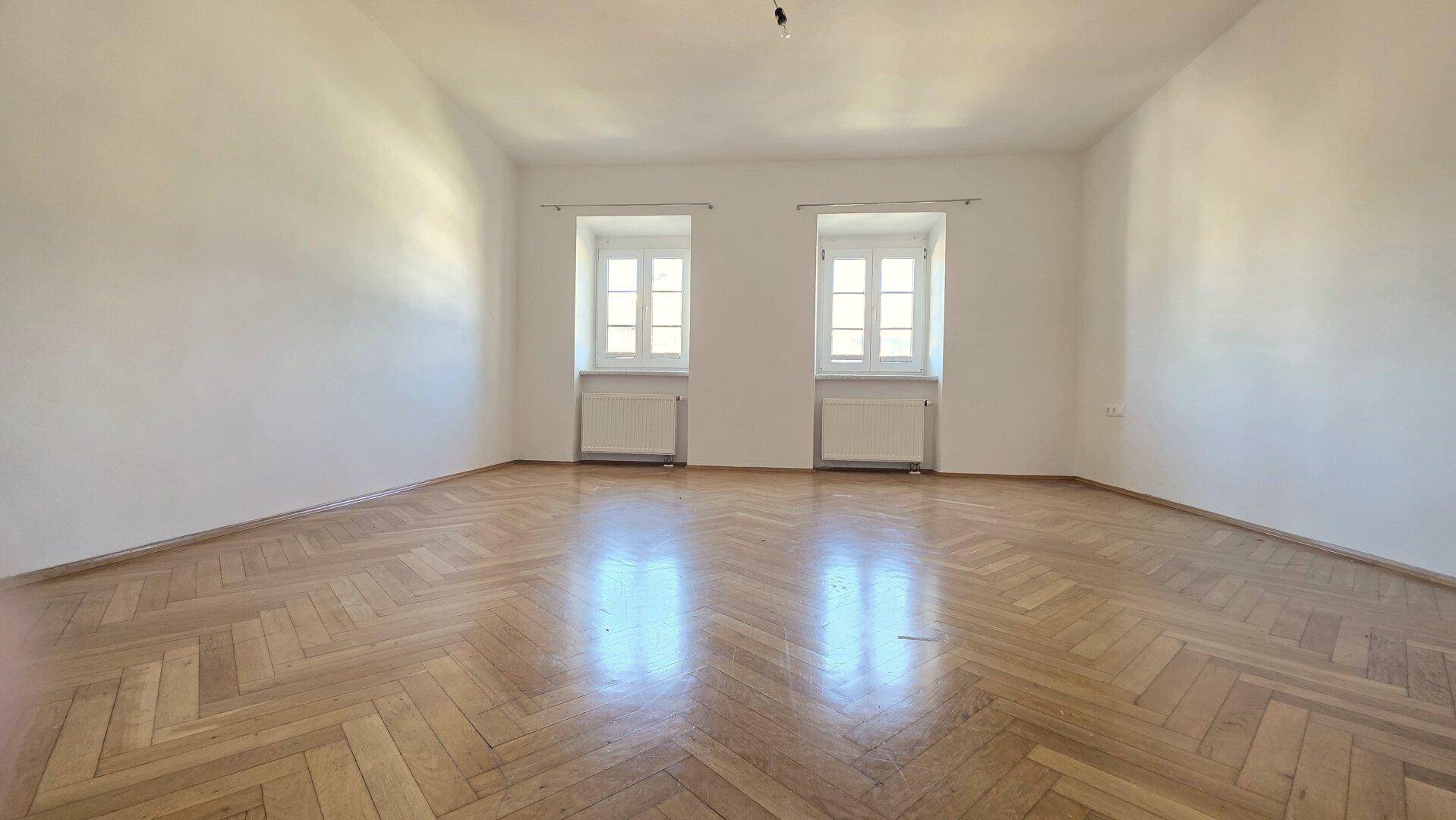 Heller Raum mit Parkettboden und zwei Fenstern, ideal als Schlaf- oder Arbeitszimmer.