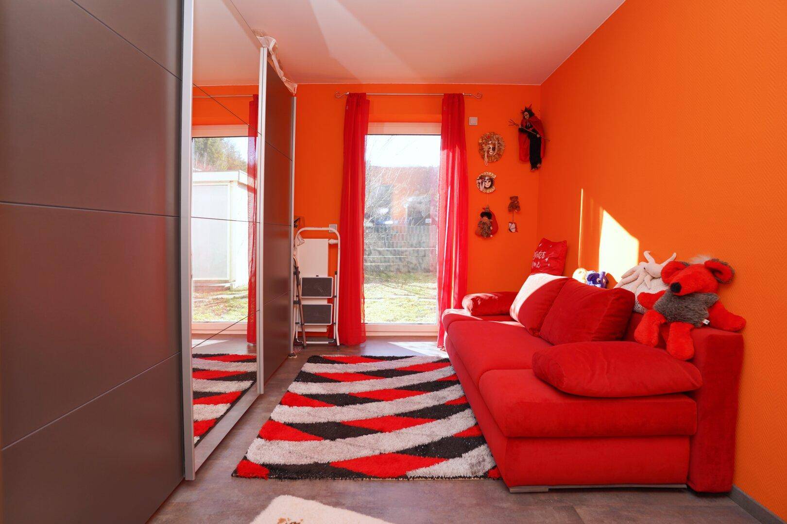 Freundliches Zimmer mit leuchtend orangefarbenen Wänden und großem Spiegelschrank.