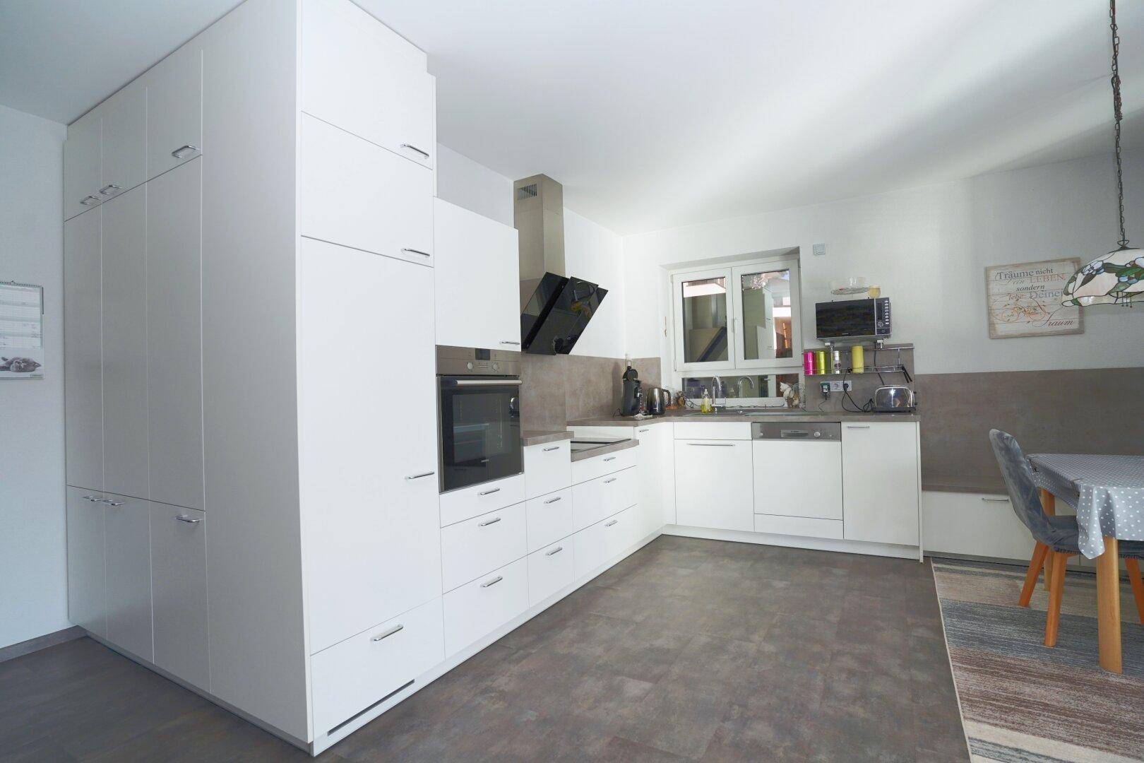 Moderne weiße Einbauküche mit viel Stauraum und Essbereich.