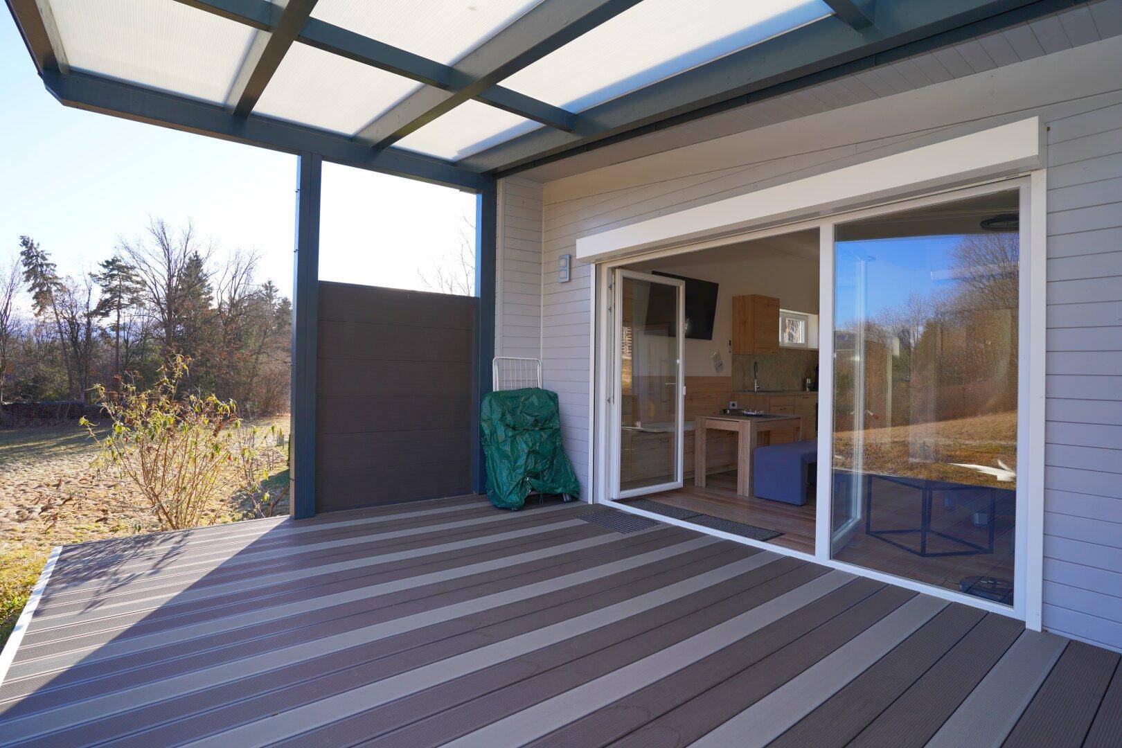 Überdachte Terrasse mit Holzboden und direktem Zugang zu einem Innenraum.