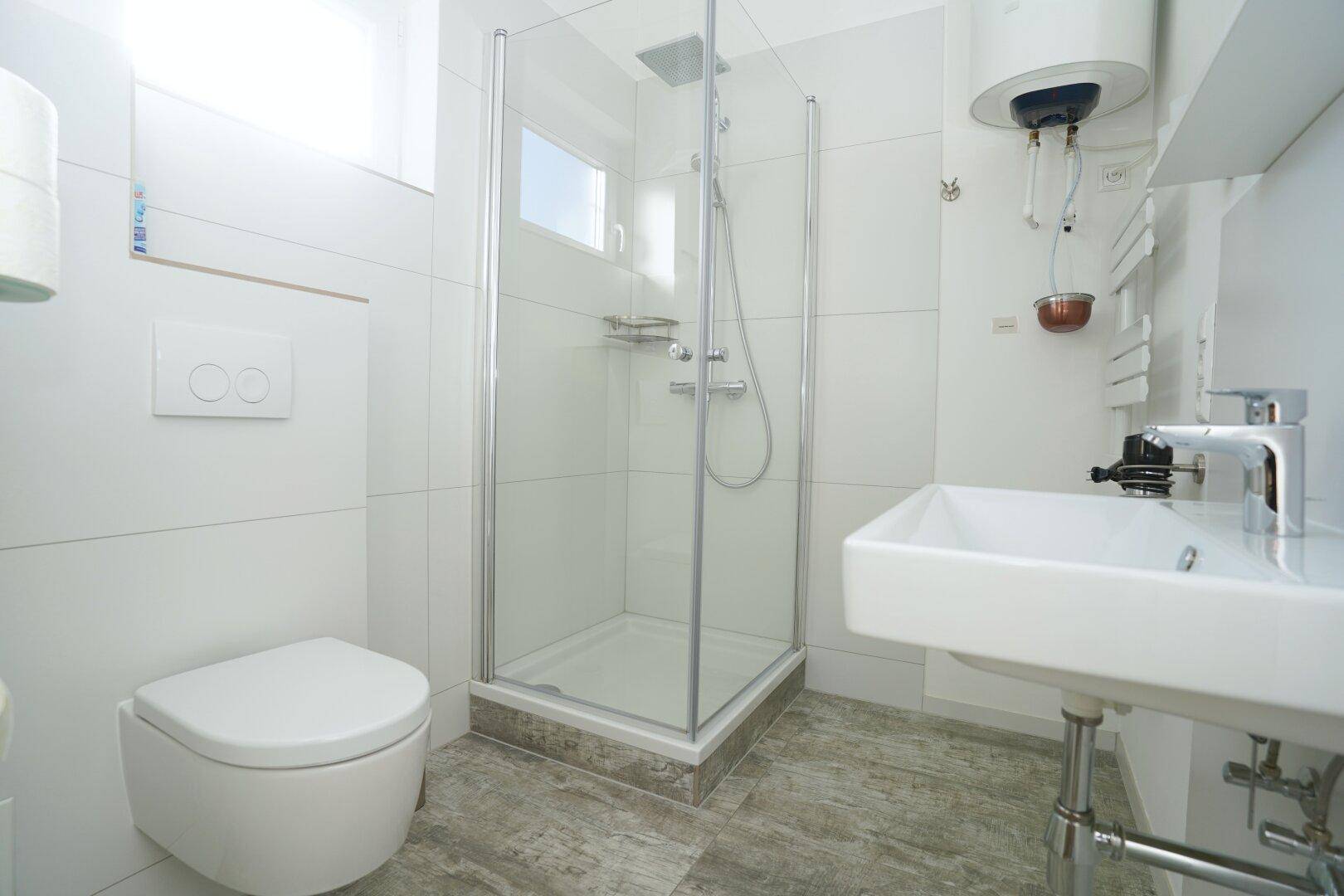 Kleines Badezimmer mit Dusche, WC und Waschbecken, hell gefliest.