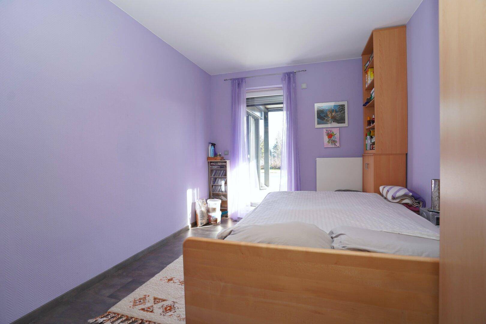 Schlafzimmer mit lila Wänden, Holzbett und Zugang zu einem Außenbereich.