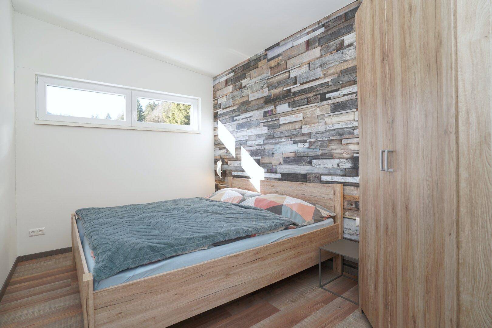 Schlafzimmer mit Holzbett und Akzentwand in Holzoptik, hell und freundlich.