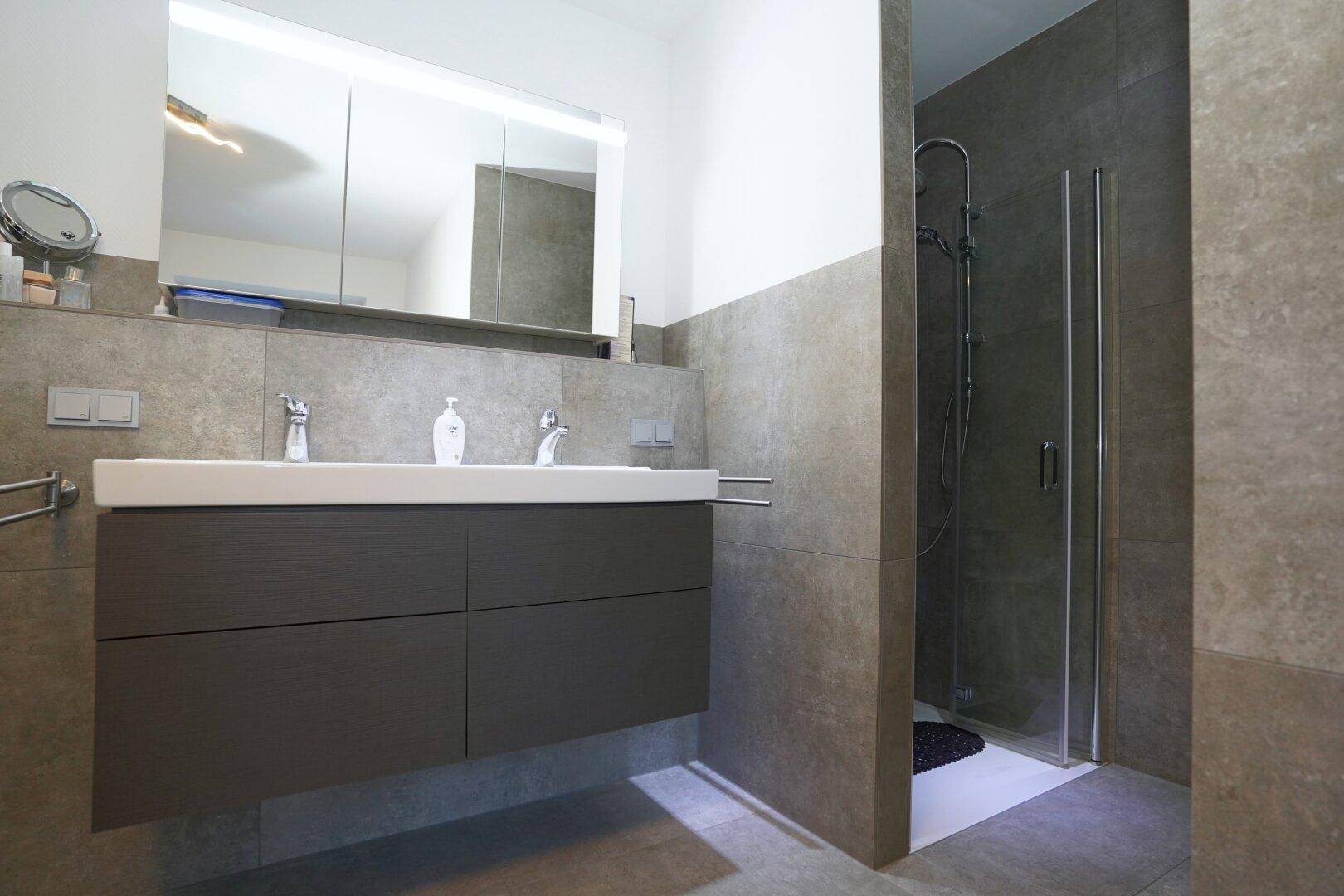 Elegantes Badezimmer mit Doppelwaschbecken, großer Dusche und modernen Fliesen.