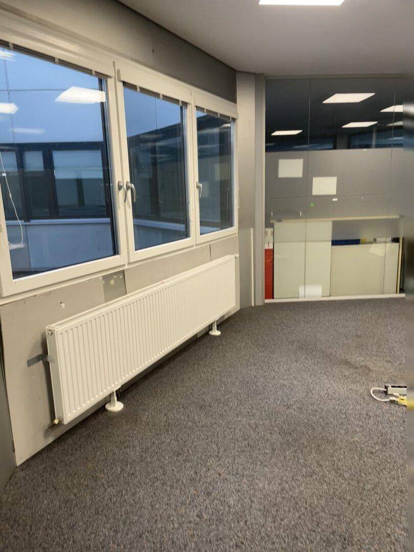 Büroraum mit breiten Fenstern, die viel Tageslicht hereinlassen, und einem langen Heizkörper.