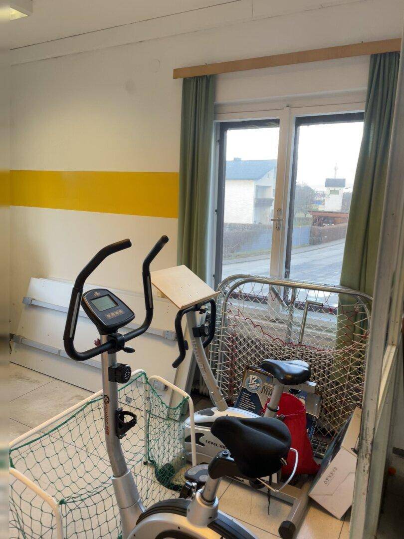 Bereich mit Fitnessgeräten, darunter ein Heimtrainer, neben einem Fenster mit Vorhängen.