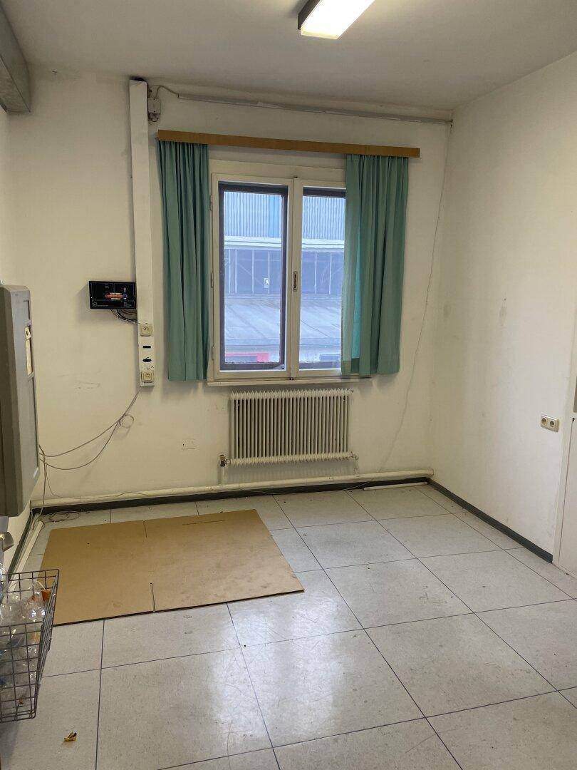 Kleiner Raum mit Fliesenboden, einem Fenster mit Vorhängen und einem Heizkörper unter der Fensterbank.