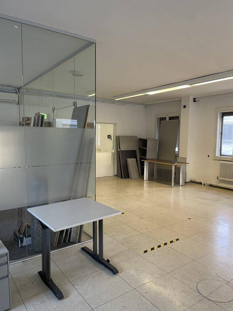 Büro mit Fliesenboden und Glasabtrennungen, die den Raum in verschiedene Arbeitsbereiche unterteilen.
