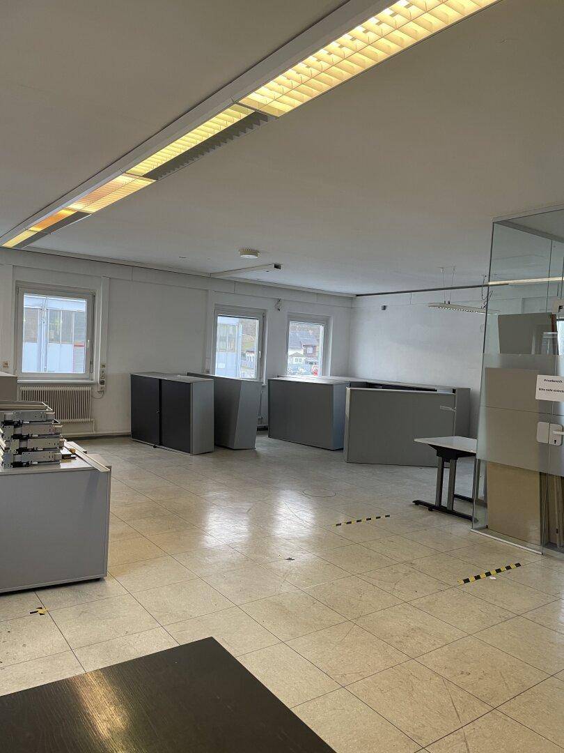 Helles Büro mit Fliesenboden, großen Fenstern und grauen Büromöbeln, bereit zur Nutzung.