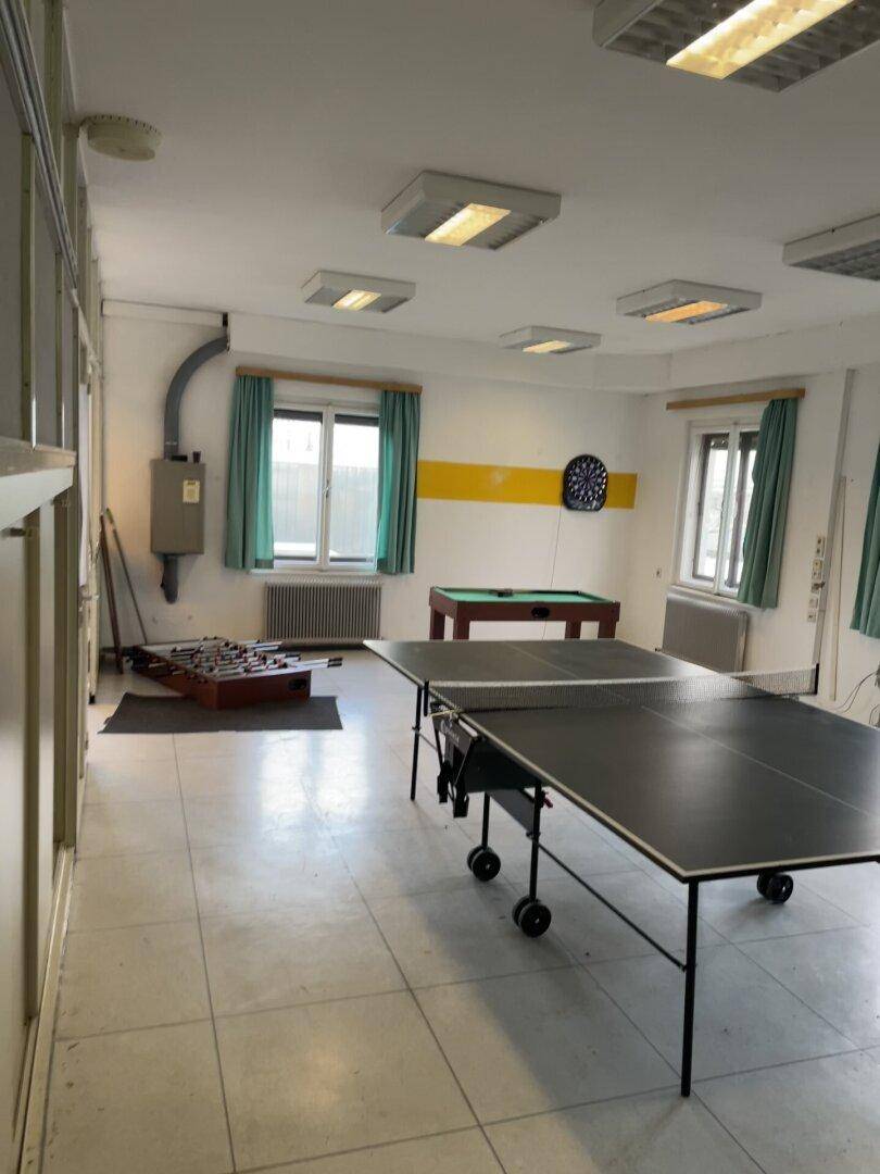 Großer Freizeitraum mit Fliesenboden, Tischtennisplatte, Billardtisch und Dartscheibe.