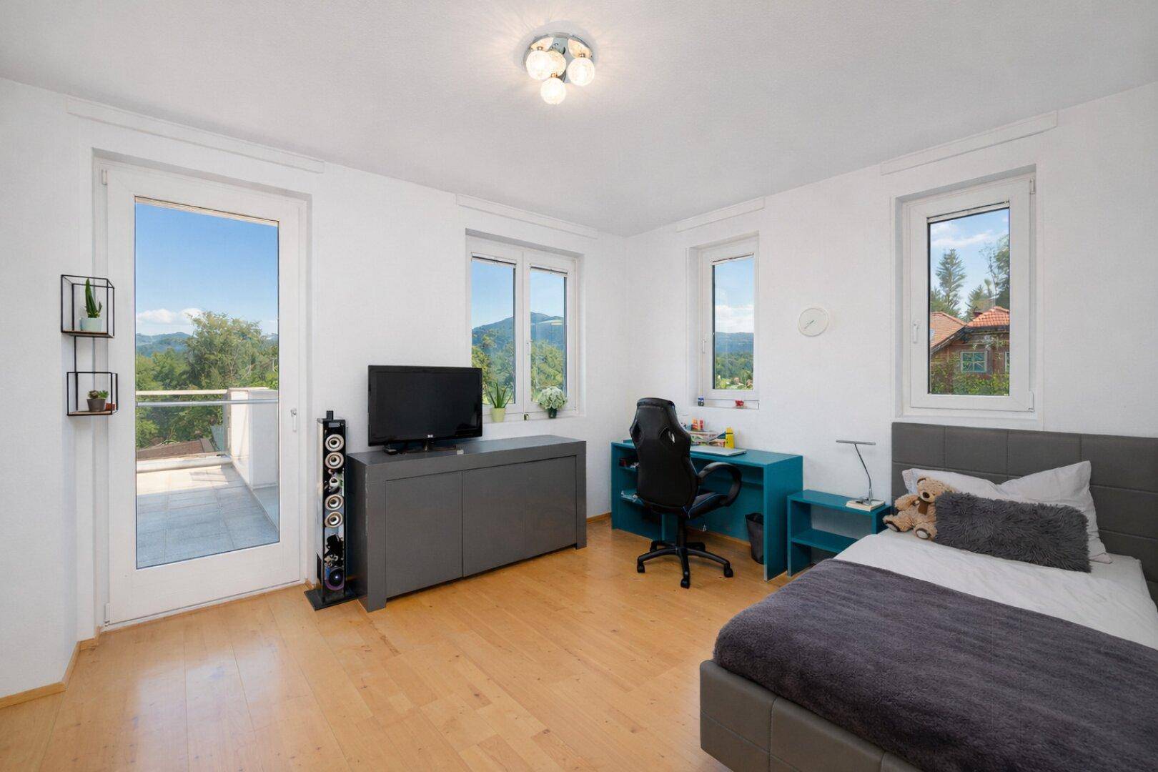 Helles Schlafzimmer mit Einzelbett, Schreibtisch und Zugang zu einem Balkon mit Aussicht.