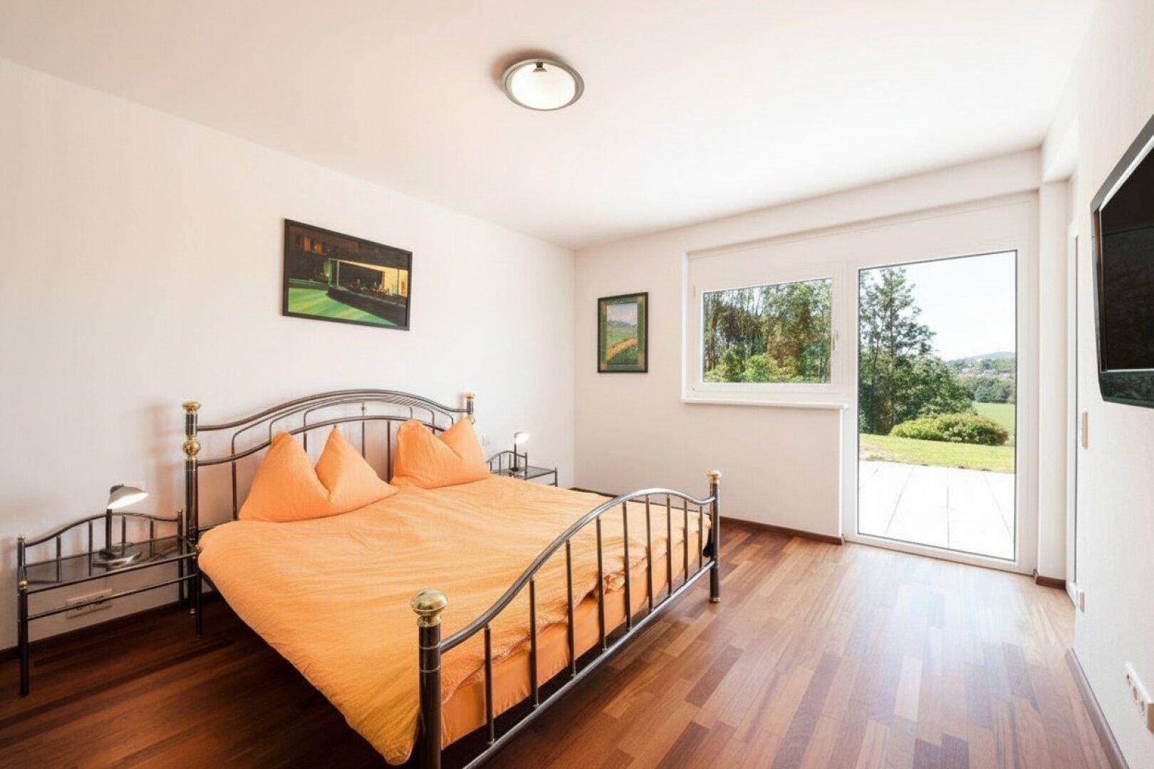 Helles Schlafzimmer mit Doppelbett, Holzboden und direktem Zugang zum Gartenbereich.