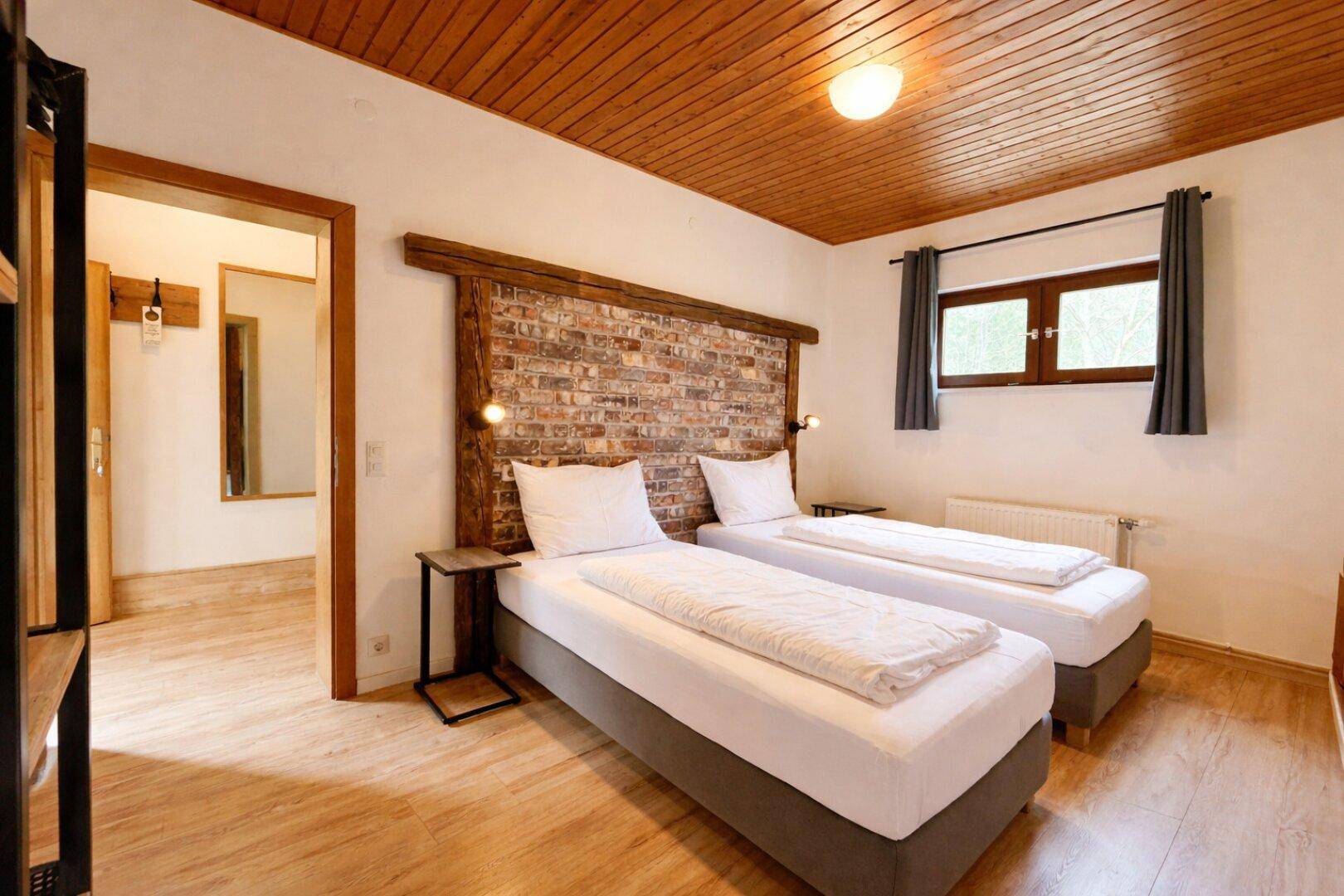 Schlafzimmer mit zwei Einzelbetten, Holzboden und Ziegelwand-Akzent.