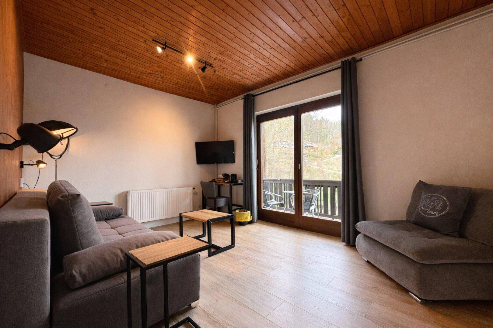 Wohnzimmer mit bequemen Sofas, Holzboden und Zugang zu einem kleinen Balkon.