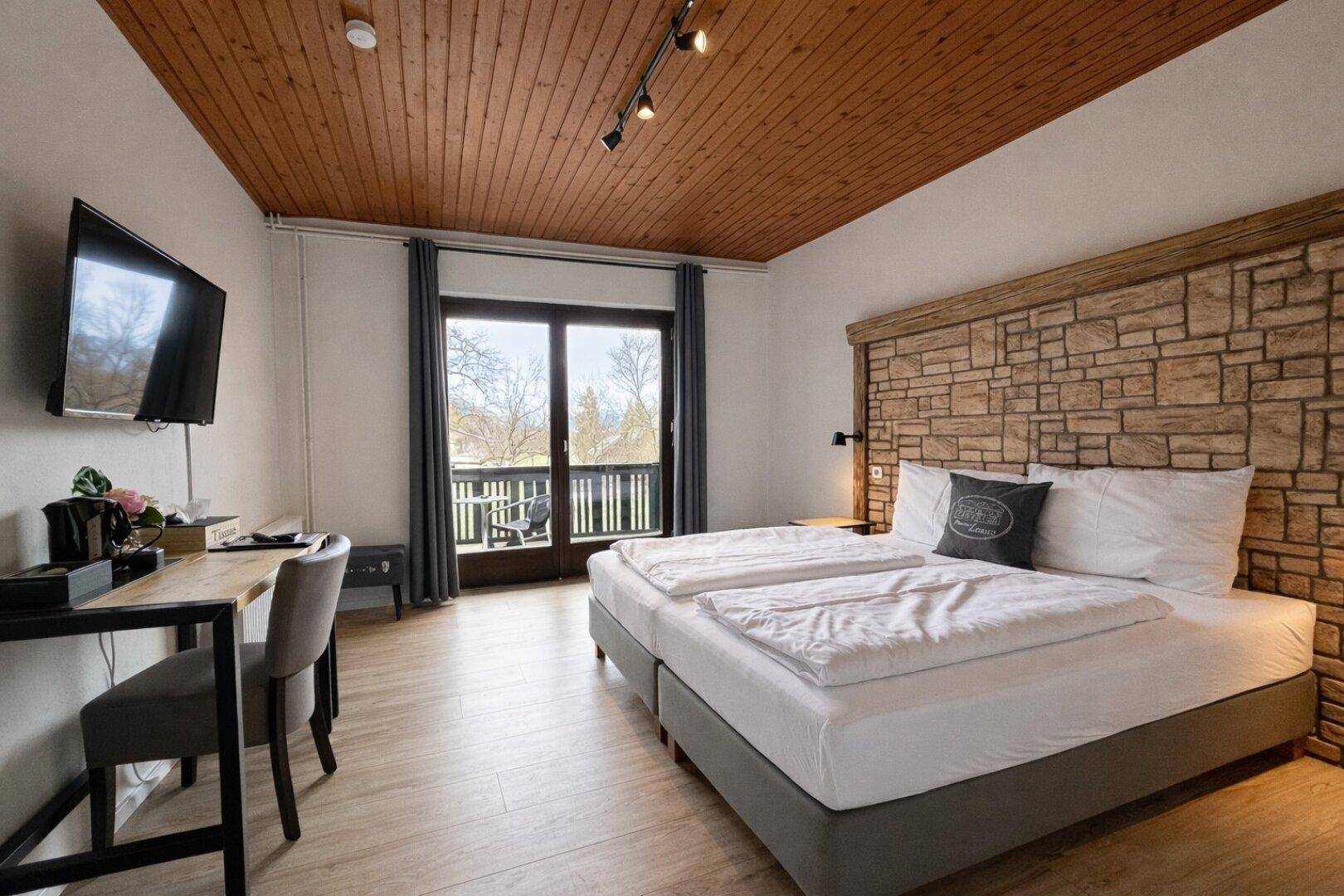 Gemütliches Schlafzimmer mit Doppelbett, Holzwand und Zugang zum Balkon.