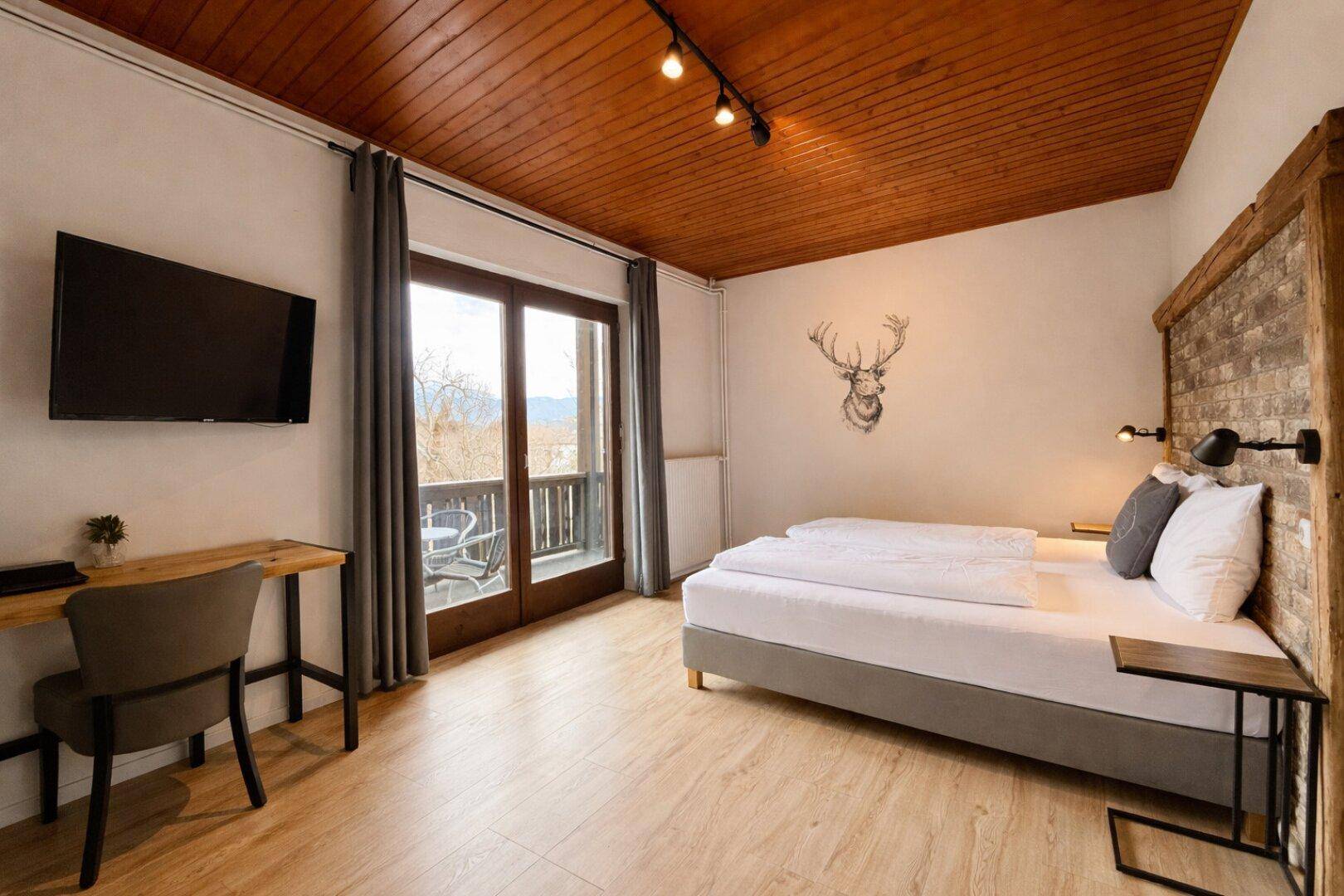 Helles Schlafzimmer mit Doppelbett, Holzwand und Balkonzugang, dekoriert mit Hirschmotiv.