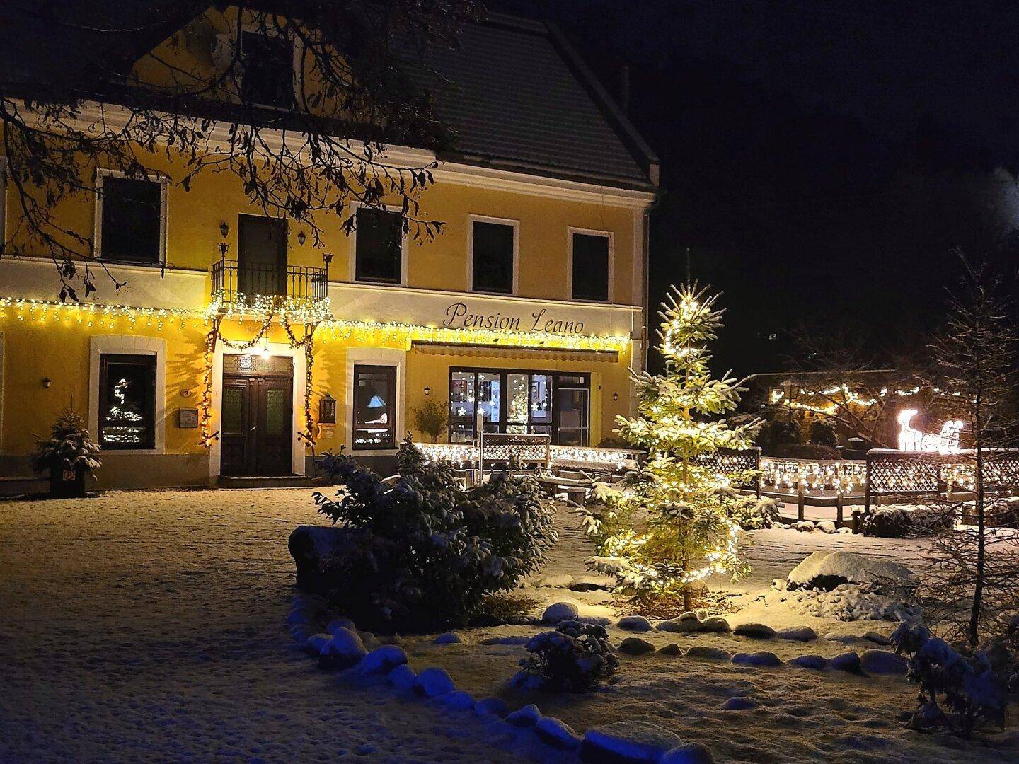 Die Pension Leano bei Nacht, festlich beleuchtet mit Weihnachtsdekoration und Schnee.