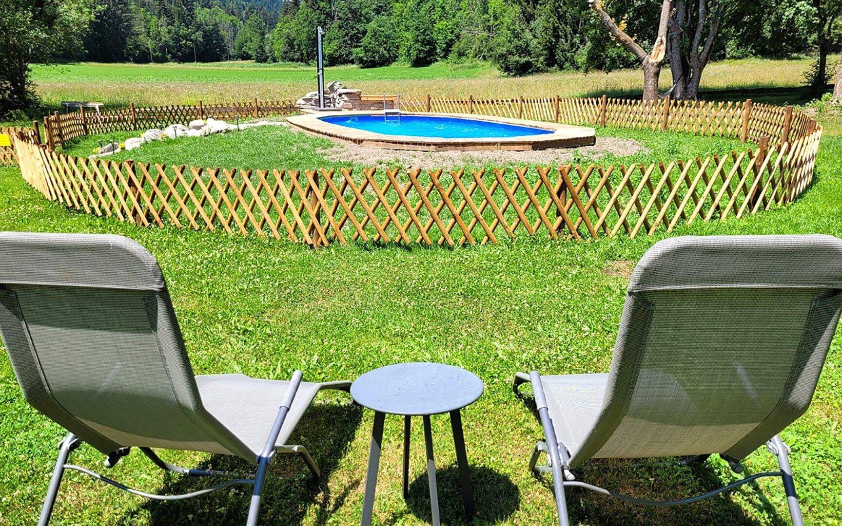 Großer Garten mit Rasenfläche, Liegestühlen und einem umzäunten Poolbereich.