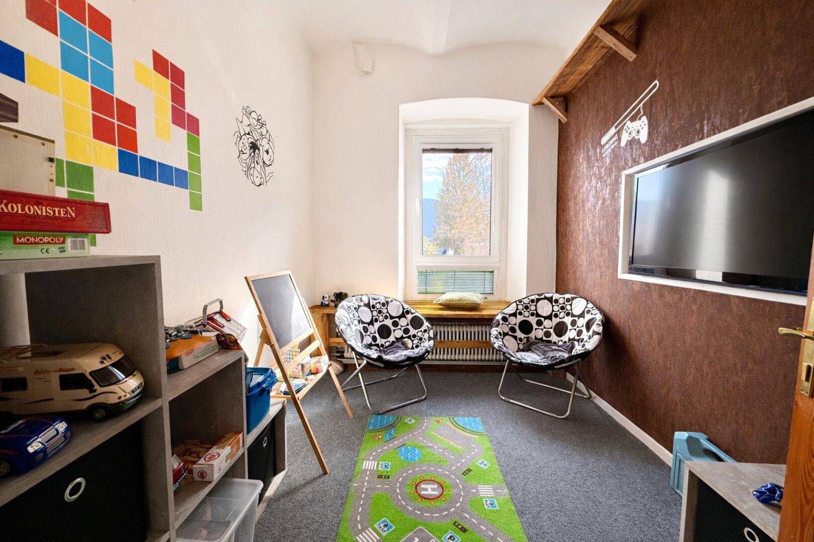 Spielzimmer mit Teppichboden, bunten Wanddekorationen und einem Fernseher.