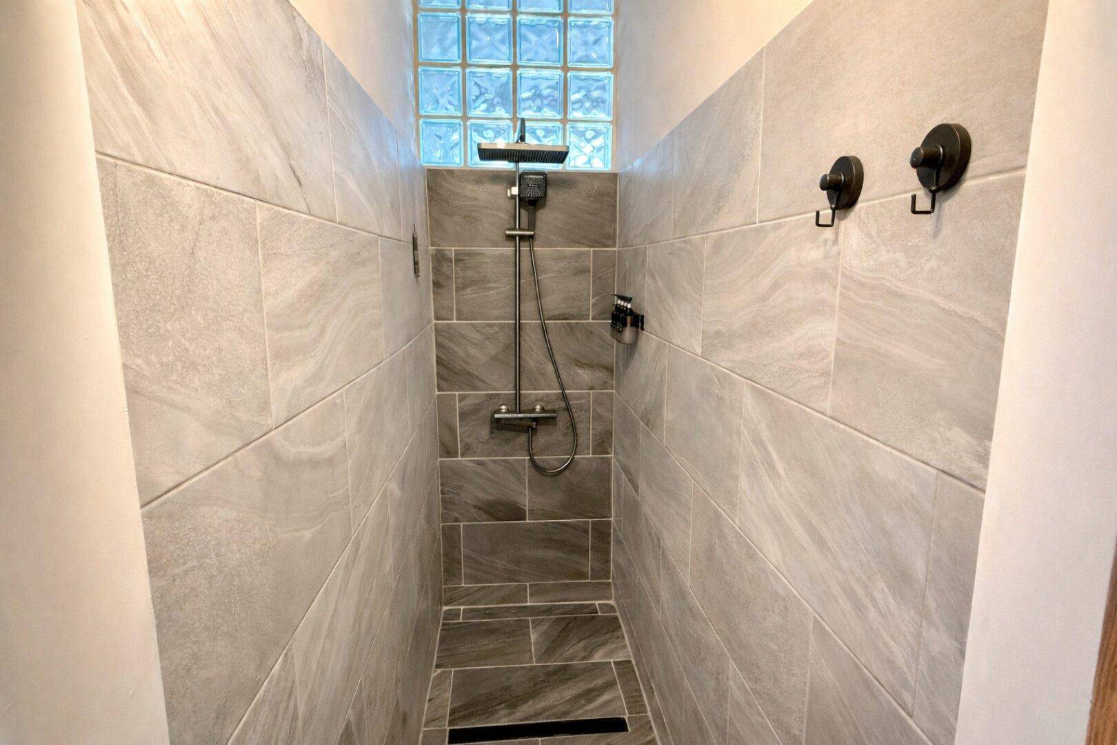 Modern geflieste Dusche mit Regenduschkopf und Glasbausteinen für natürliches Licht.
