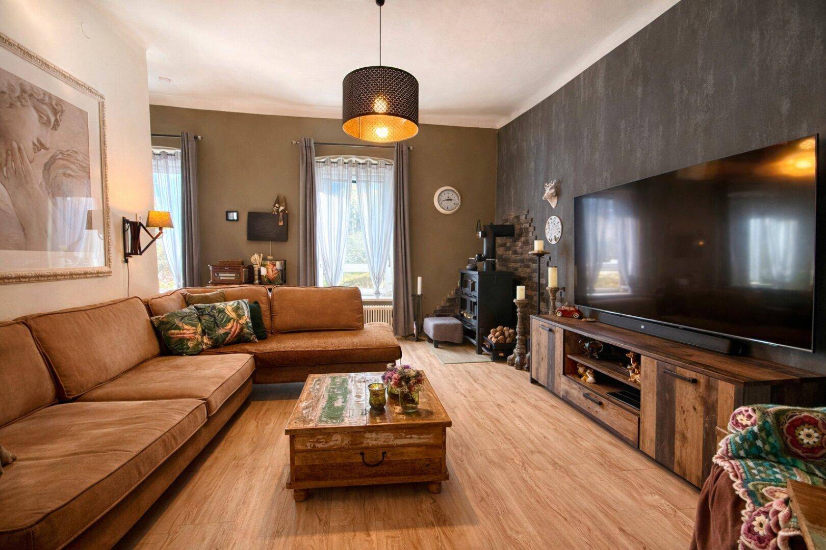 Großzügiges Wohnzimmer mit Ecksofa, Holzboden und Kaminofen.