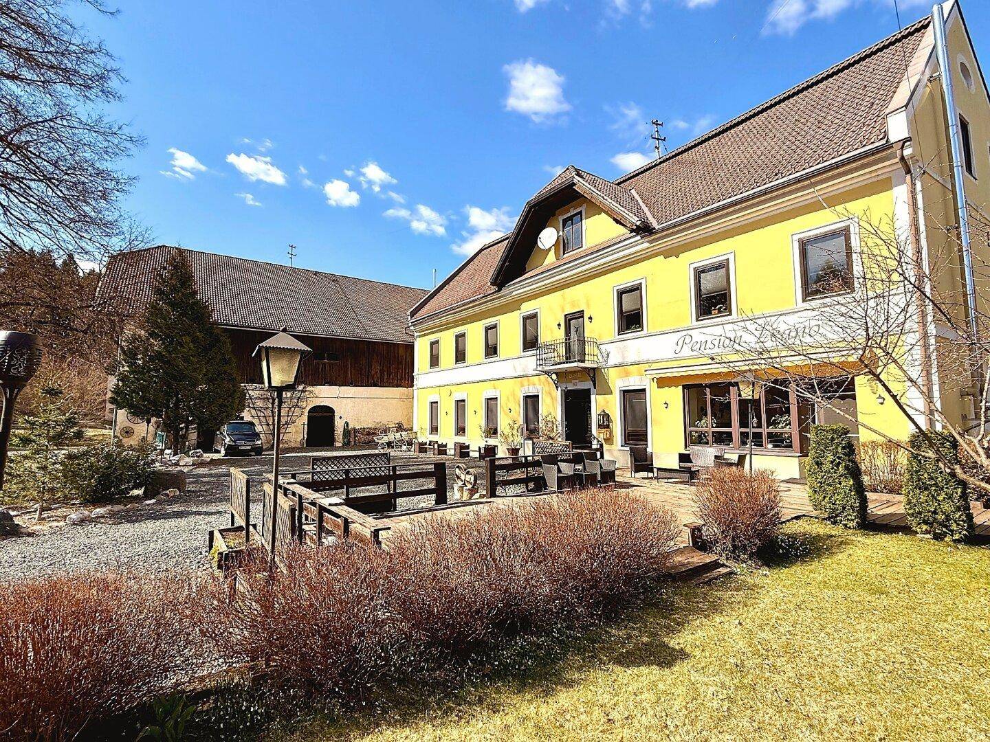 Weitläufige Ansicht der gelben Pension Leano mit großem Vorplatz und angrenzendem Gebäude.