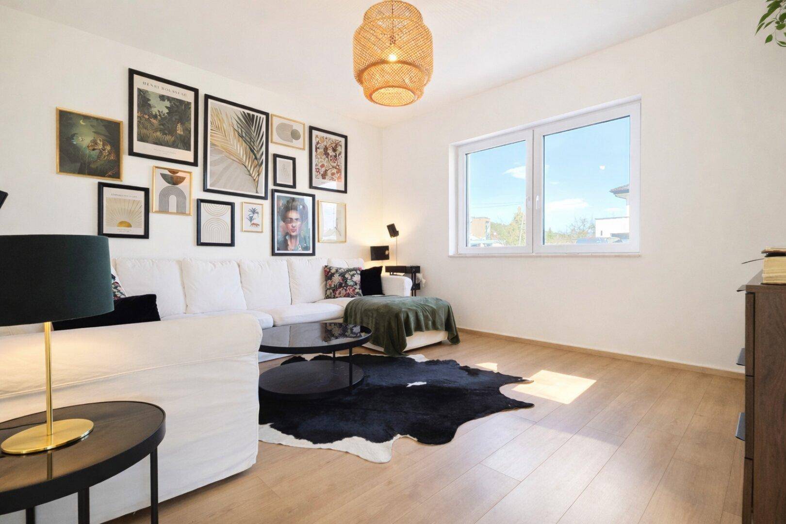 Gemütliches Wohnzimmer mit weißem Sofa, Holzboden und einer dekorativen Bilderwand.