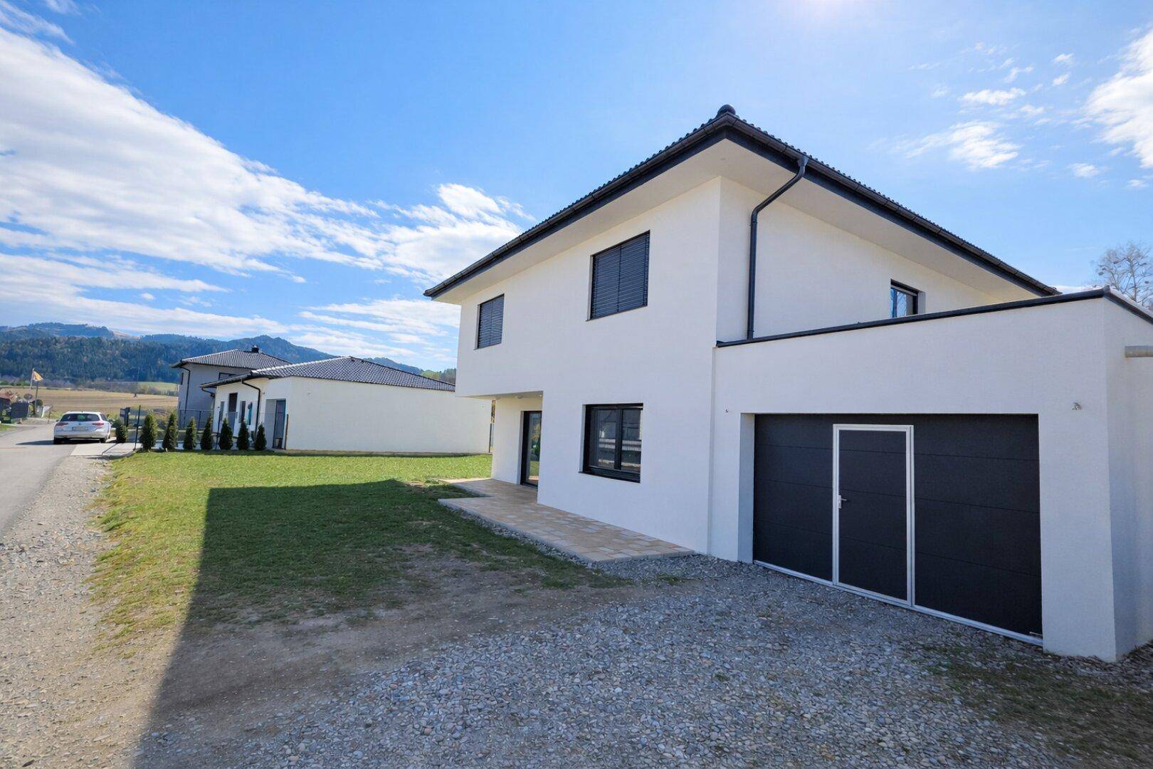 Neubau-Einfamilienhaus mit integrierter Garage, weißer Fassade und Schotterauffahrt.