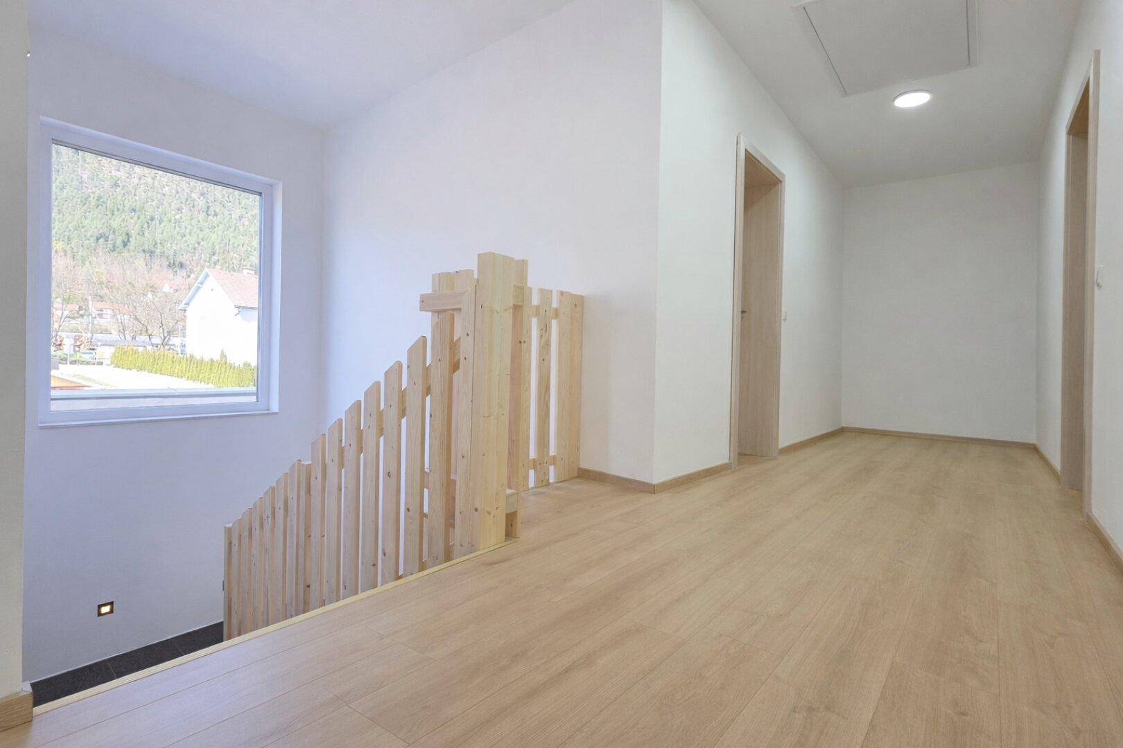 Heller Flur im Obergeschoss mit Holzgeländer und Fenster mit Blick ins Grüne.