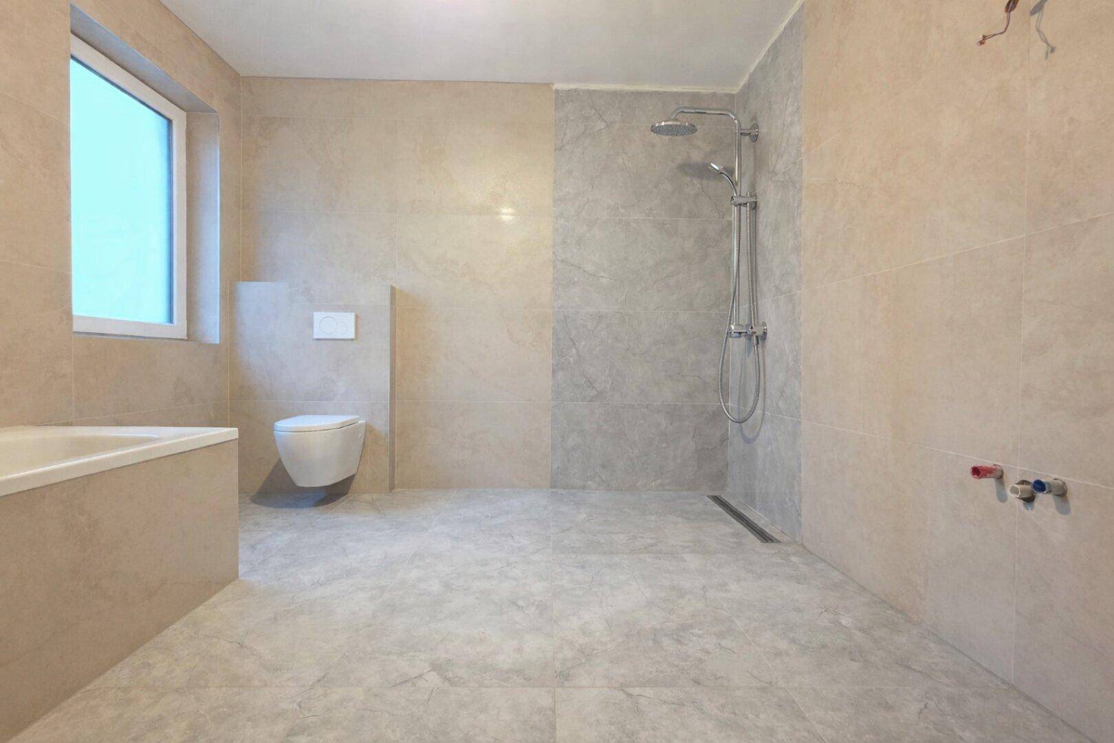 Geräumiges Badezimmer in neutralen Fliesenfarben mit Badewanne, Dusche und Fenster.