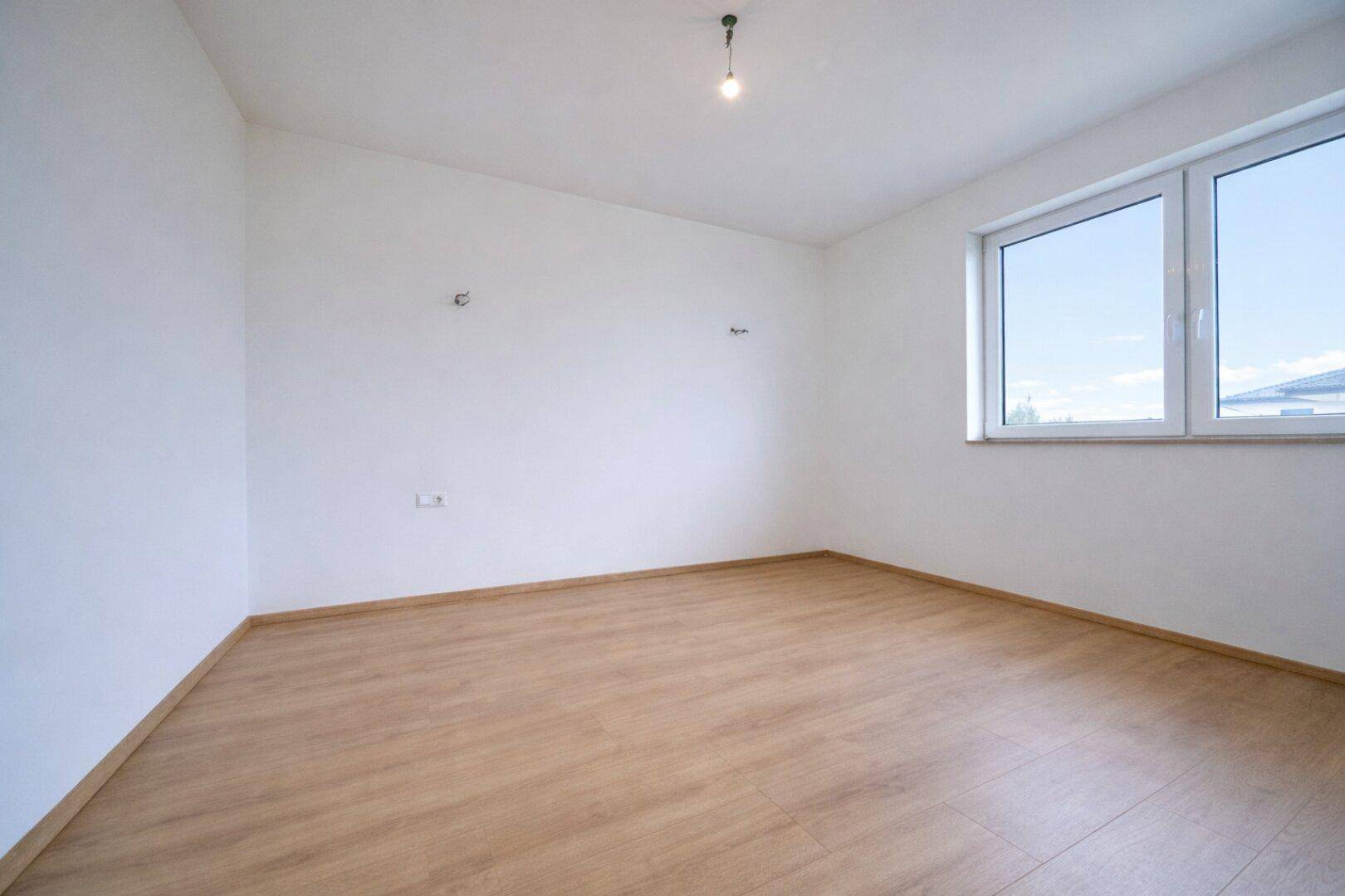 Leeres Schlafzimmer mit hellem Laminatboden und zwei Fenstern für viel Tageslicht.
