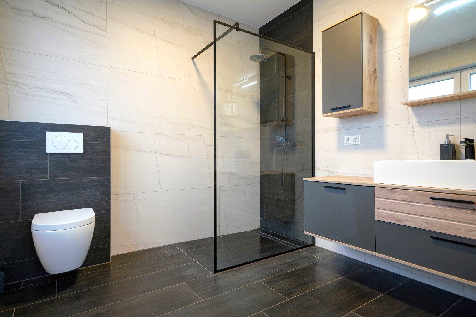 Modernes Badezimmer mit dunklen und hellen Fliesen, begehbarer Dusche und Waschtisch.