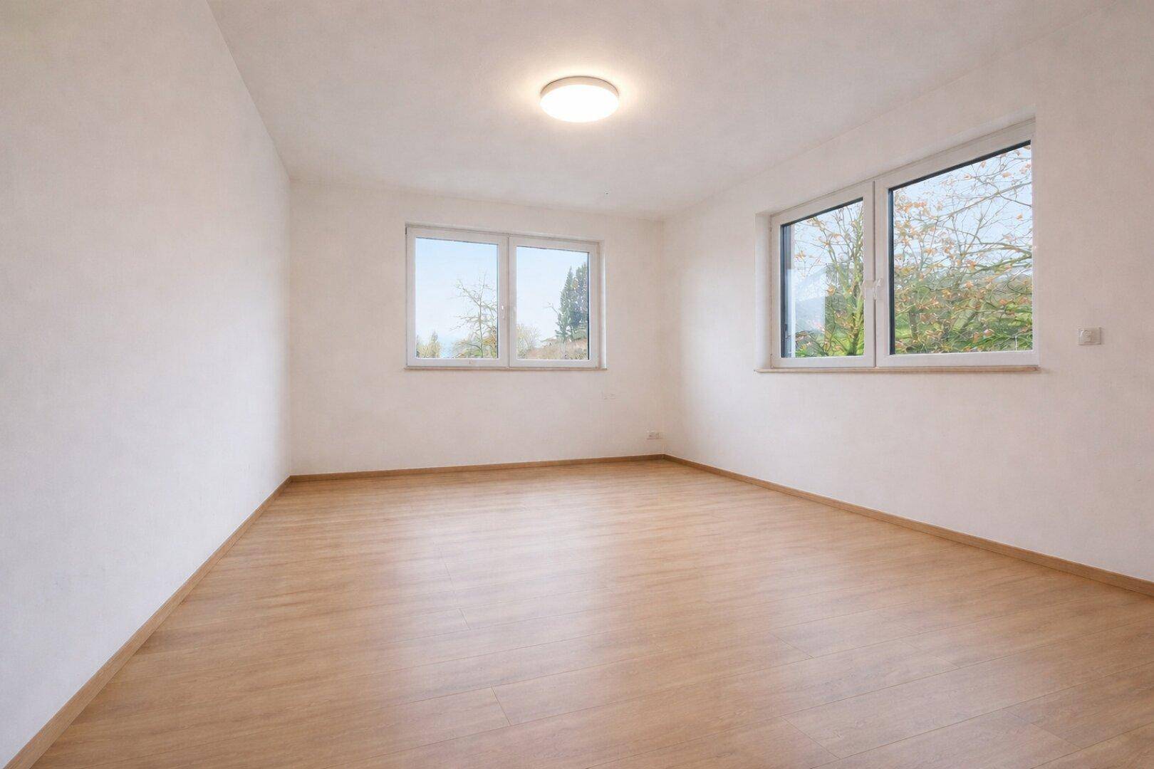 Geräumiges, leeres Zimmer mit hellem Laminatboden und mehreren Fenstern.