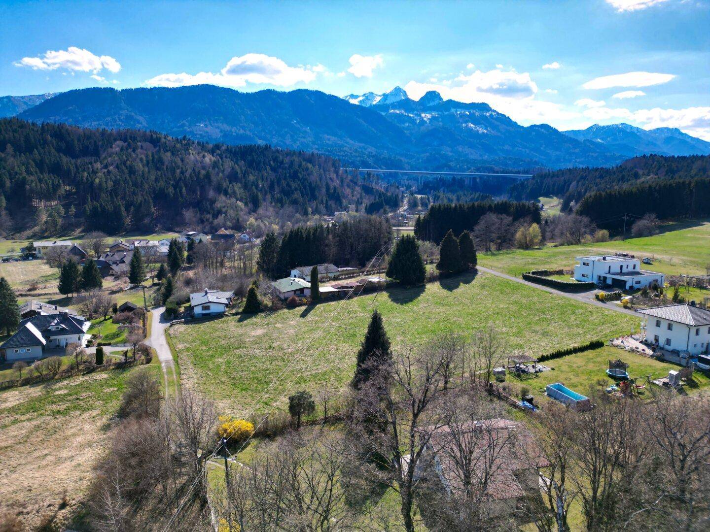 Panoramablick aus der Vogelperspektive auf die grüne Landschaft mit Bergen und einer Brücke in der Ferne.