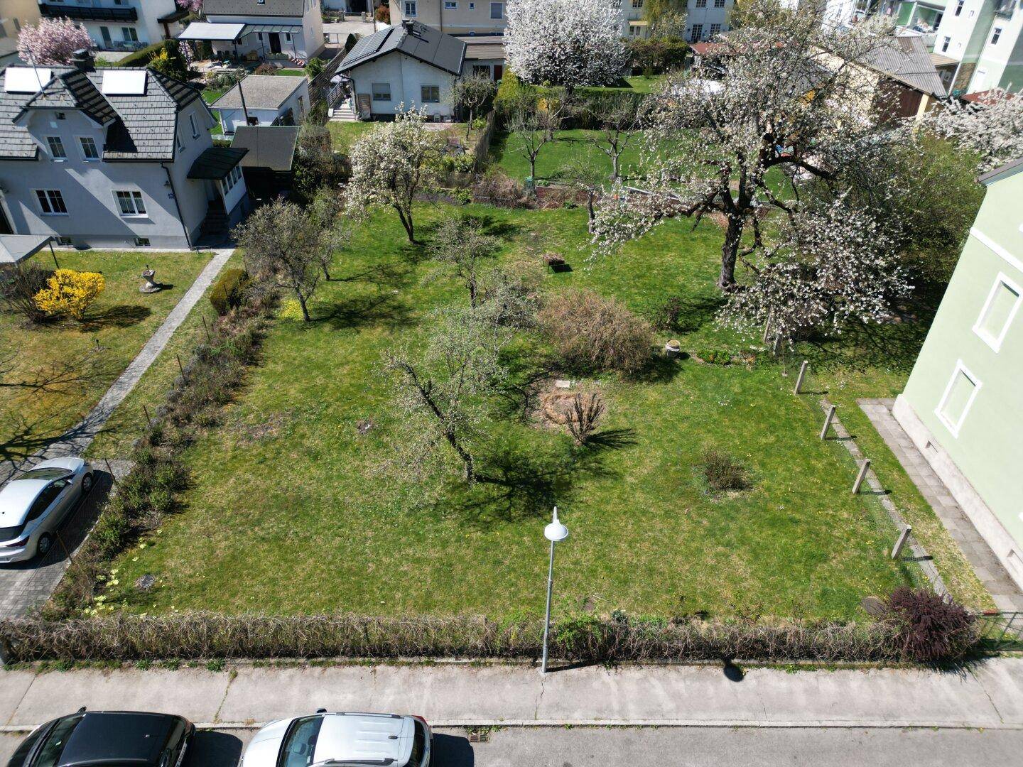 Luftaufnahme des Grundstücks mit Rasenfläche, umgeben von einer Hecke und der angrenzenden Straße.