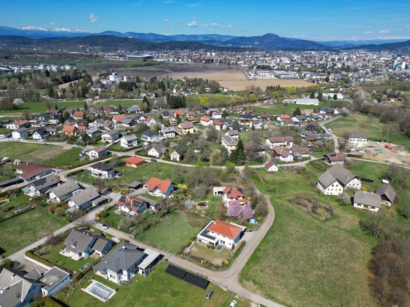 Weitläufige Luftaufnahme eines Wohngebiets eingebettet in eine grüne Landschaft mit Bergen im Hintergrund.