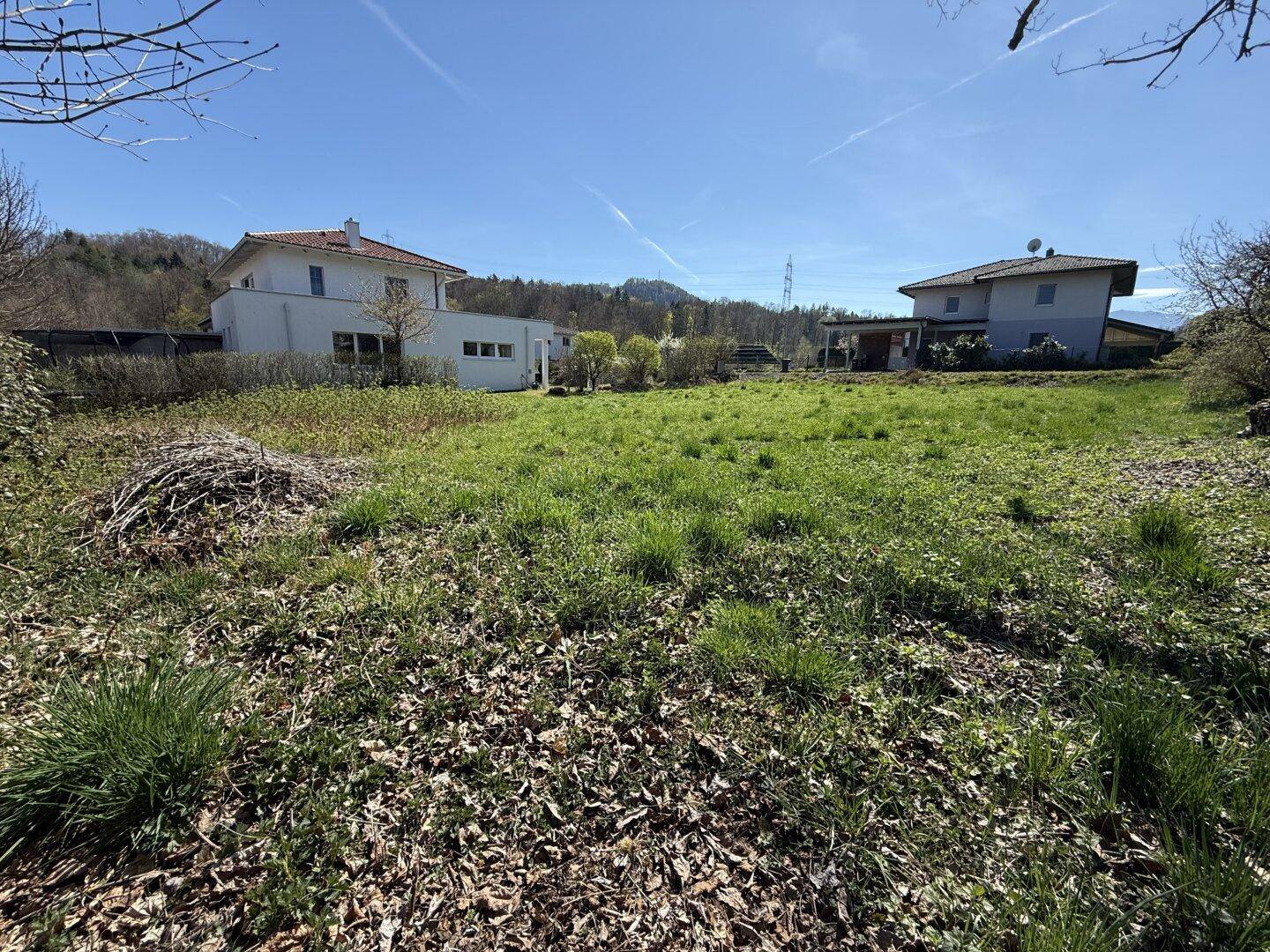 Weitläufiges, sonniges Grundstück mit Grasfläche und Blick auf die Nachbarhäuser und die Landschaft.
