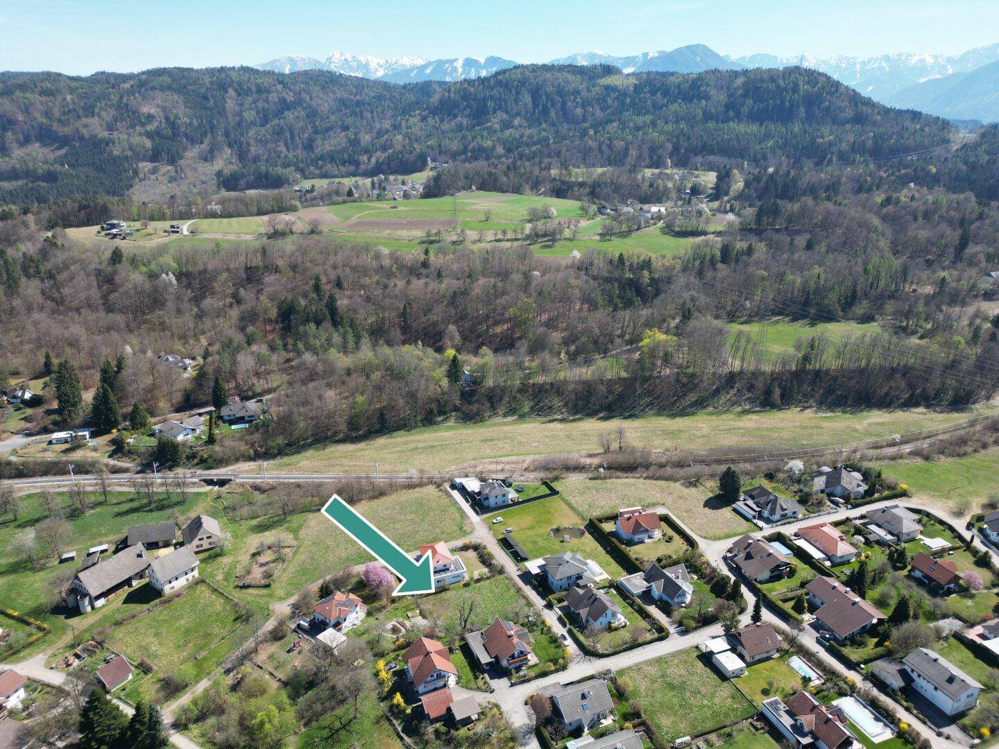 Panoramische Luftaufnahme eines Wohngebiets mit einem markierten Grundstück und bewaldeten Hügeln.