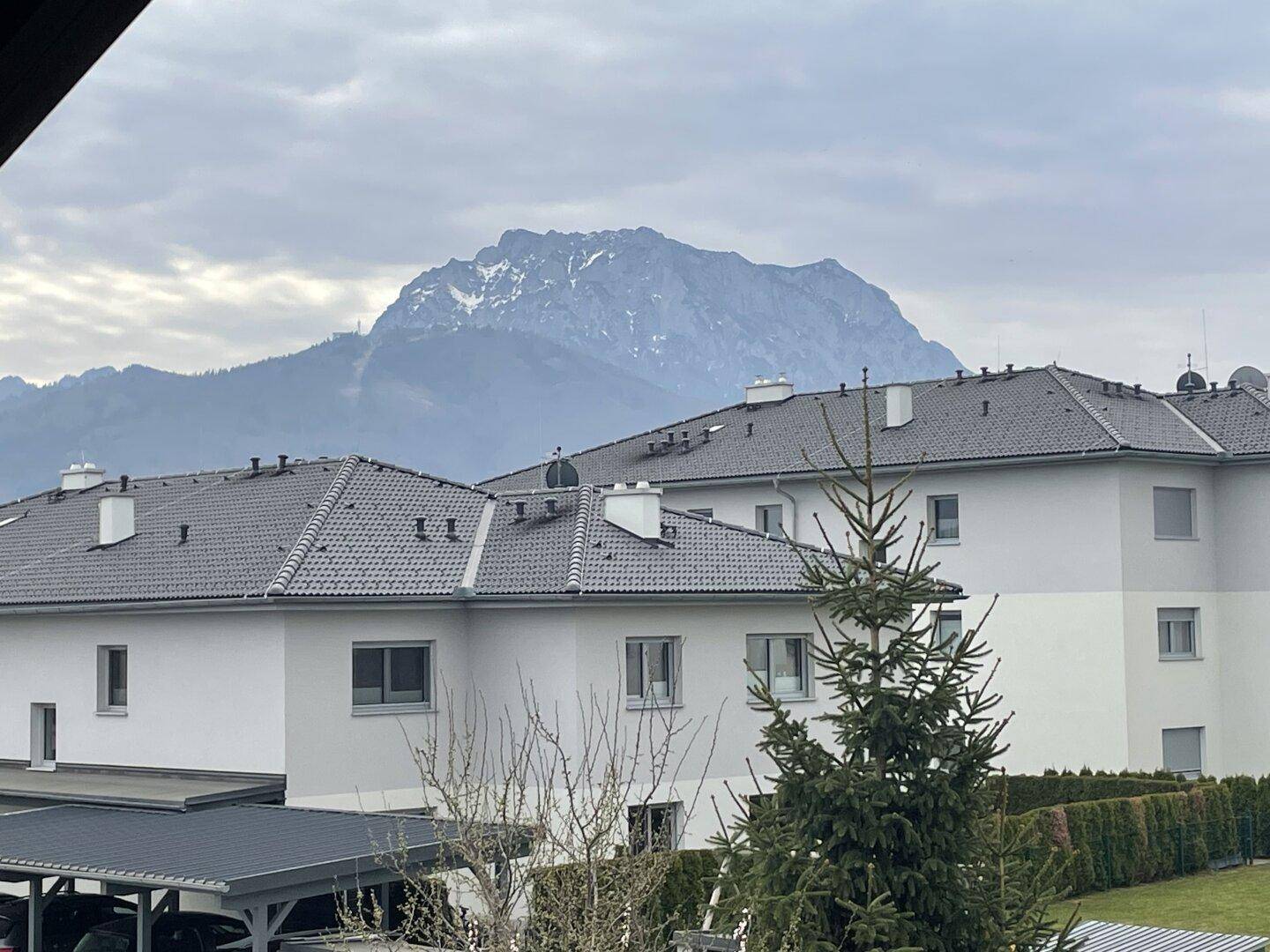 Panoramablick auf schneebedeckte Berge über den Dächern benachbarter Häuser.