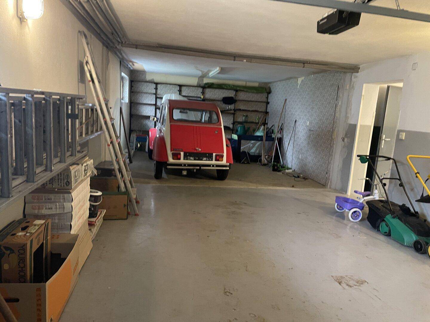 Geräumige Garage mit Betonboden, Lagerregalen und einem Oldtimer als Blickfang.