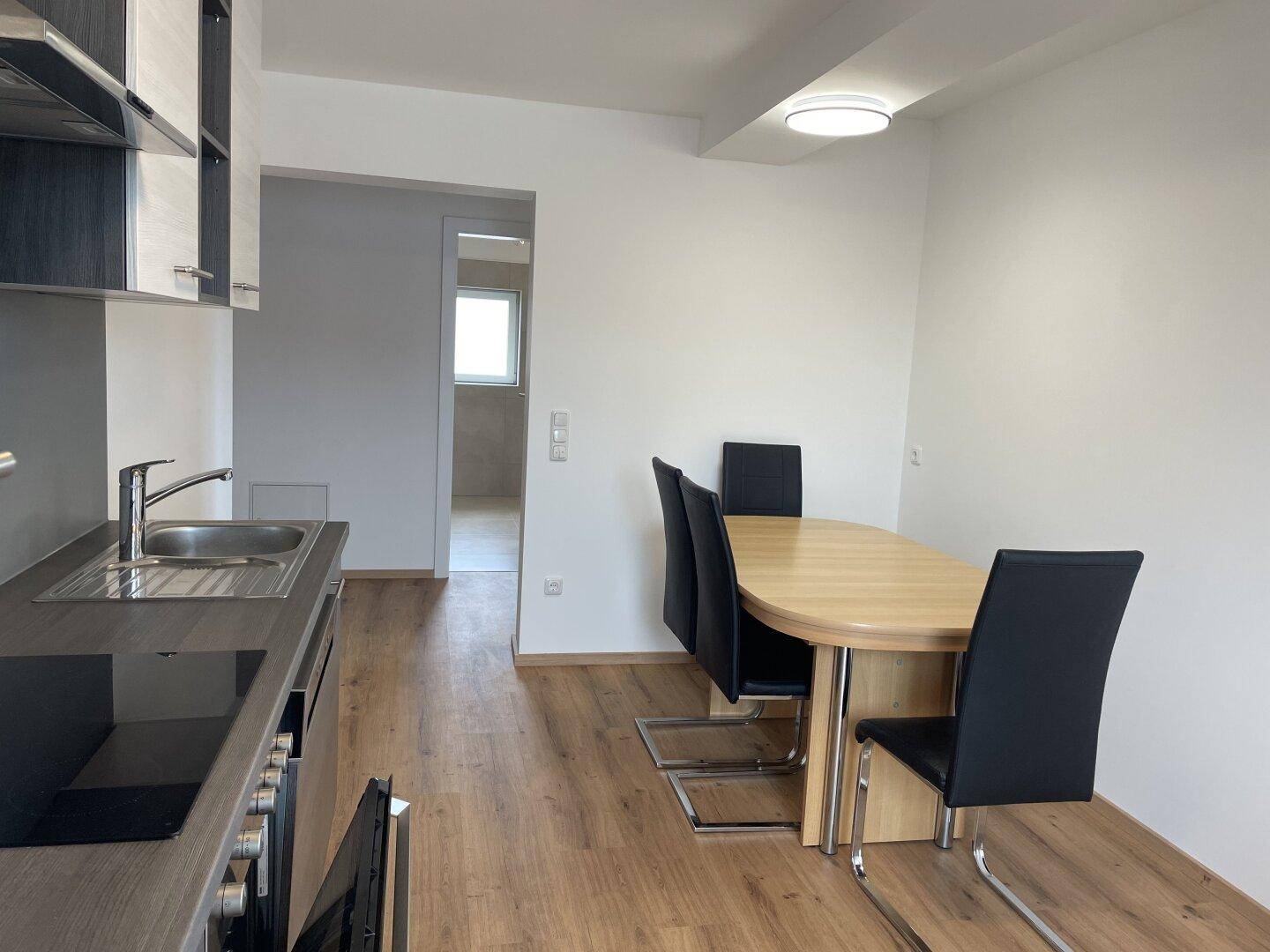 Moderne Einbauküche mit Essbereich, dunklen Arbeitsplatten und hellem Holzboden.