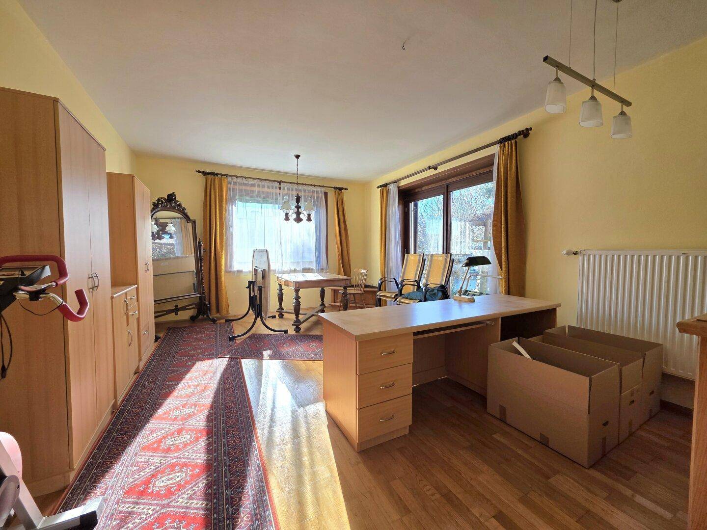 Heller Wohnraum mit Schreibtisch, Holzschränken und Teppich auf Parkettboden.