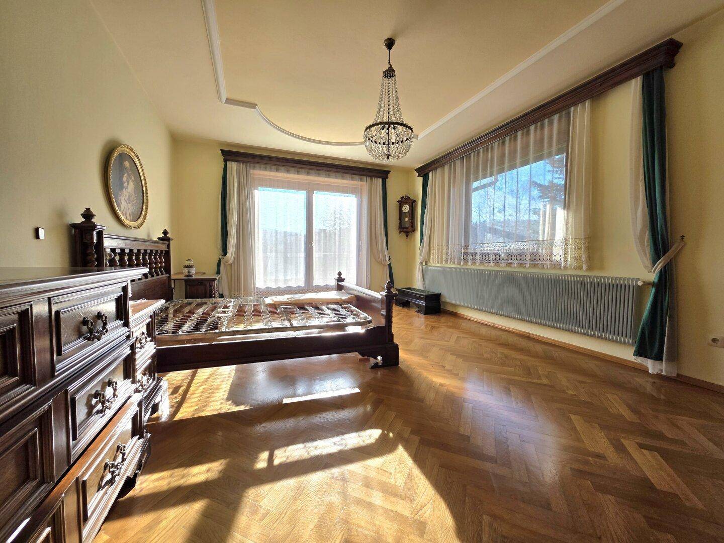 Elegantes Schlafzimmer mit antikem Holzmöbeln, Kronleuchter und Parkettboden.