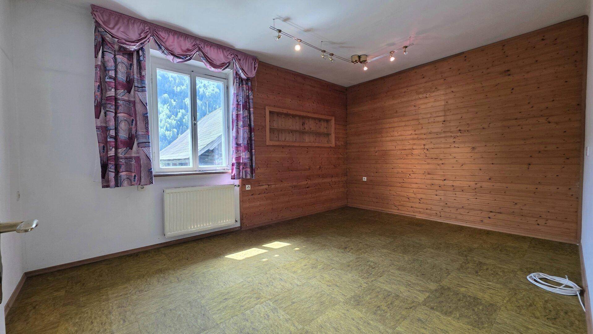 Leerer Raum mit Holzvertäfelung an einer Wand, grünem Boden und einem Fenster.