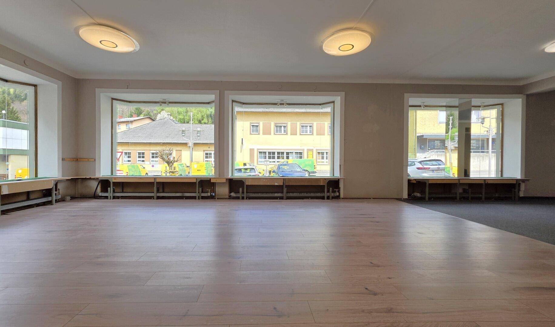 Heller, leerer Raum mit Holzboden und großen Fenstern, die viel Tageslicht hereinlassen.